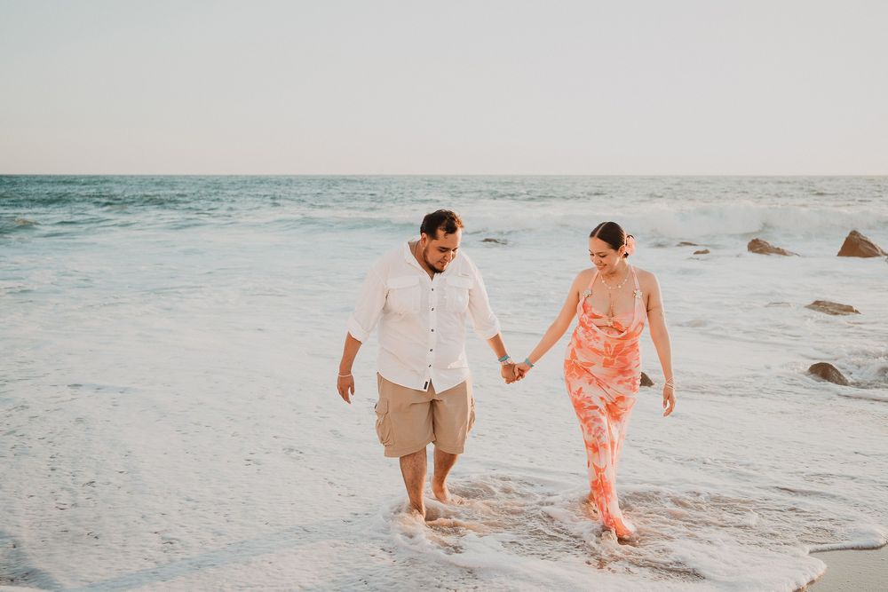 Pareja caminando tomada de la mano por la orilla del mar durante una sesión de pareja en Mazatlán.