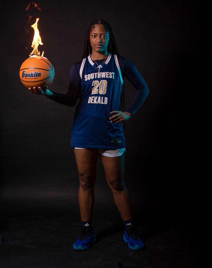 Basketball player in blue uniform holds flaming basketball in dramatic studio photo.
