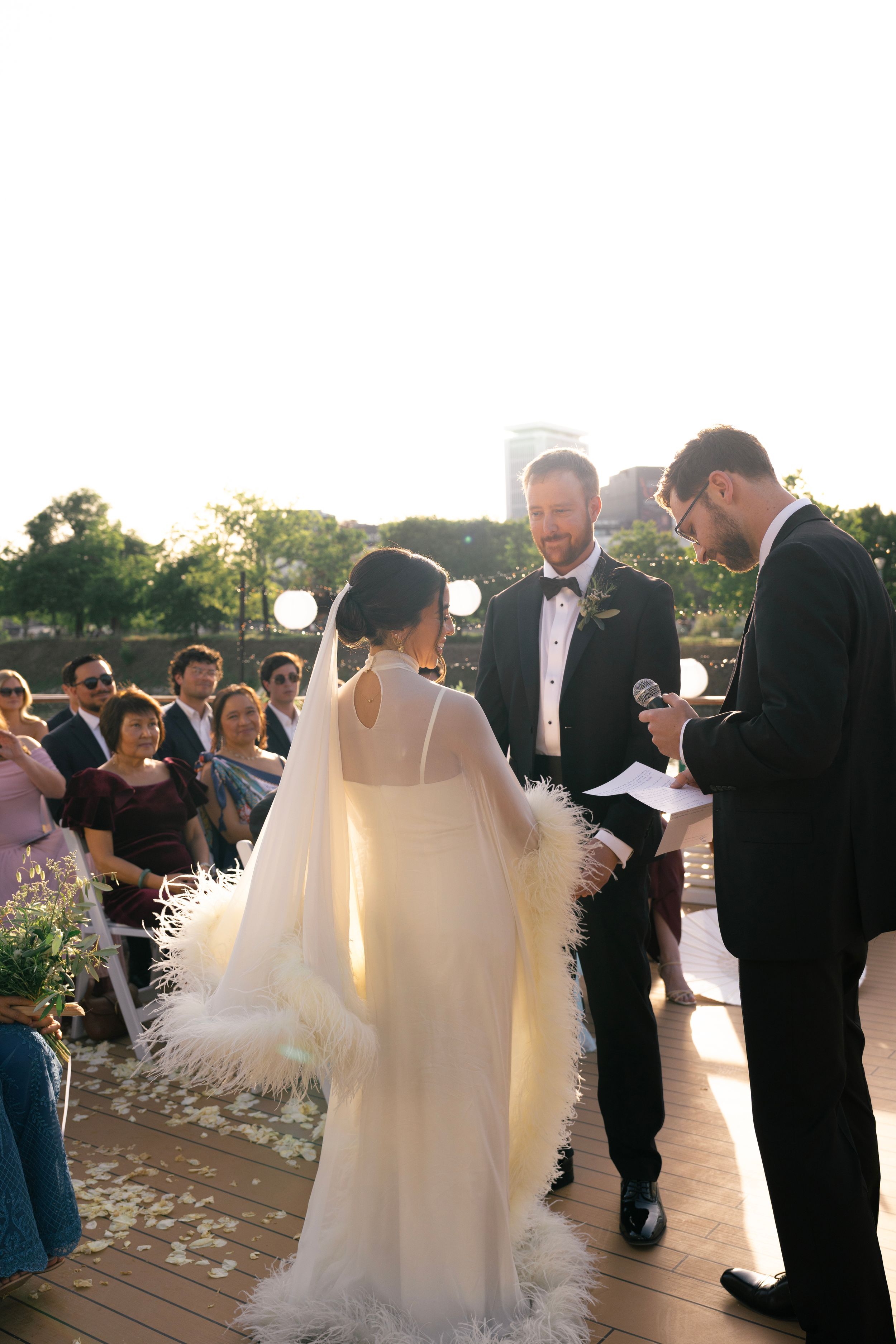 Bride in feather-trimmed cape wedding dress stands on seine river cruise wedding at golden hour, paris wedding venue, paris wedding ceremony