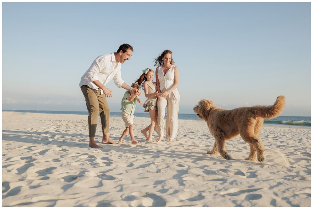 Happy family with golden retriever dog plays together on white sandy beach at sunset.