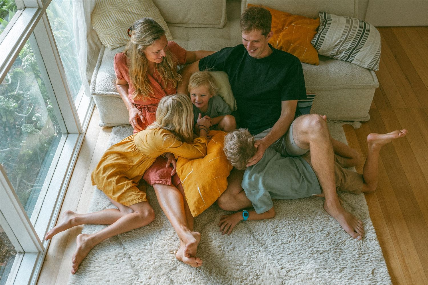 Three happy children with blue eyes cuddle together, smiling warmly on a cozy white couch.