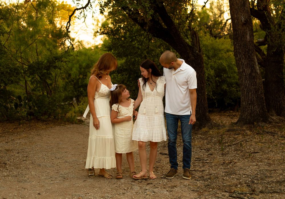Family of four sharing a warm moment together on a sunlit dirt path surrounded by trees.