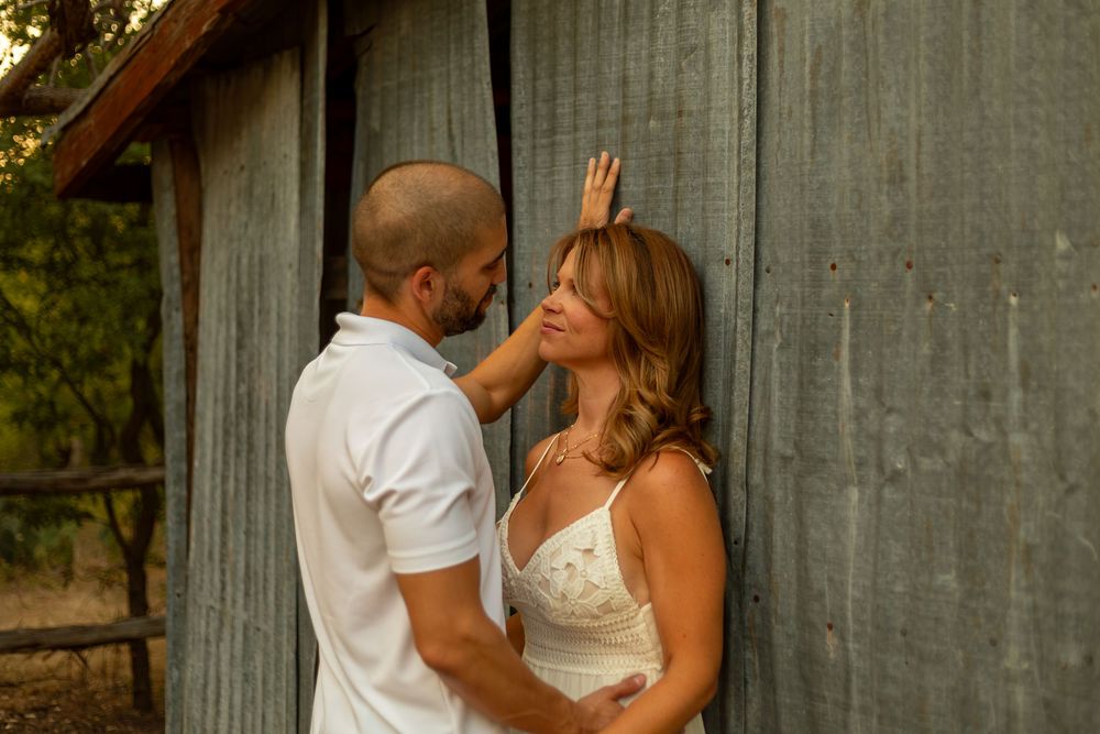 Couple sharing a tender moment by a rustic wooden barn wall, man gently touching woman's hair outdoors.