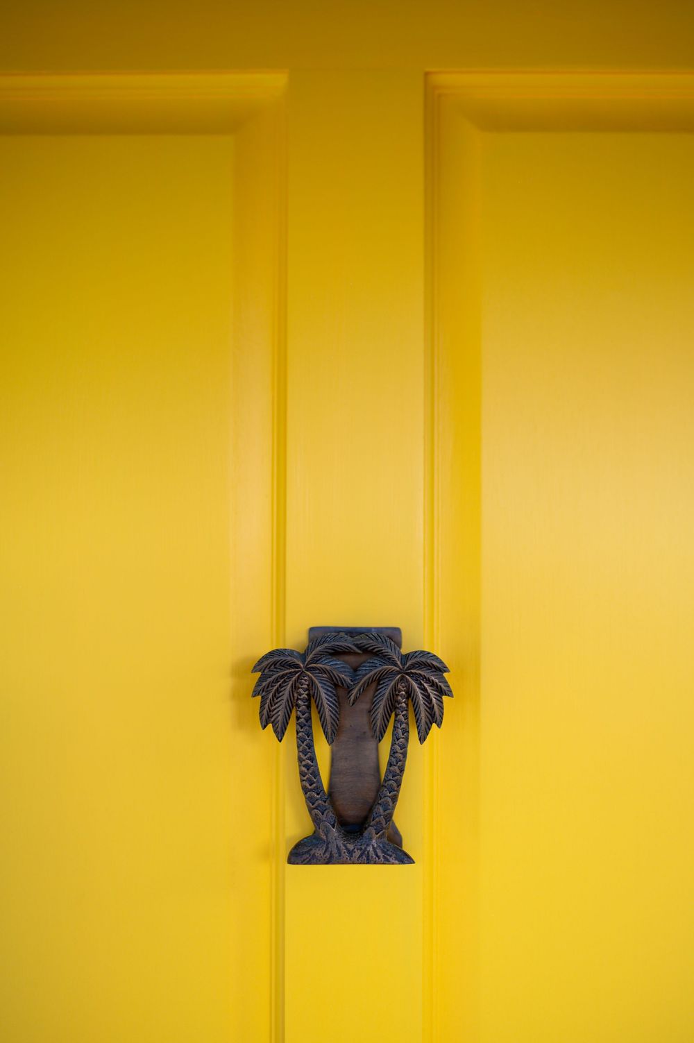 Bright yellow door with decorative black cast iron palm tree door knocker, tropical coastal home exterior detail.