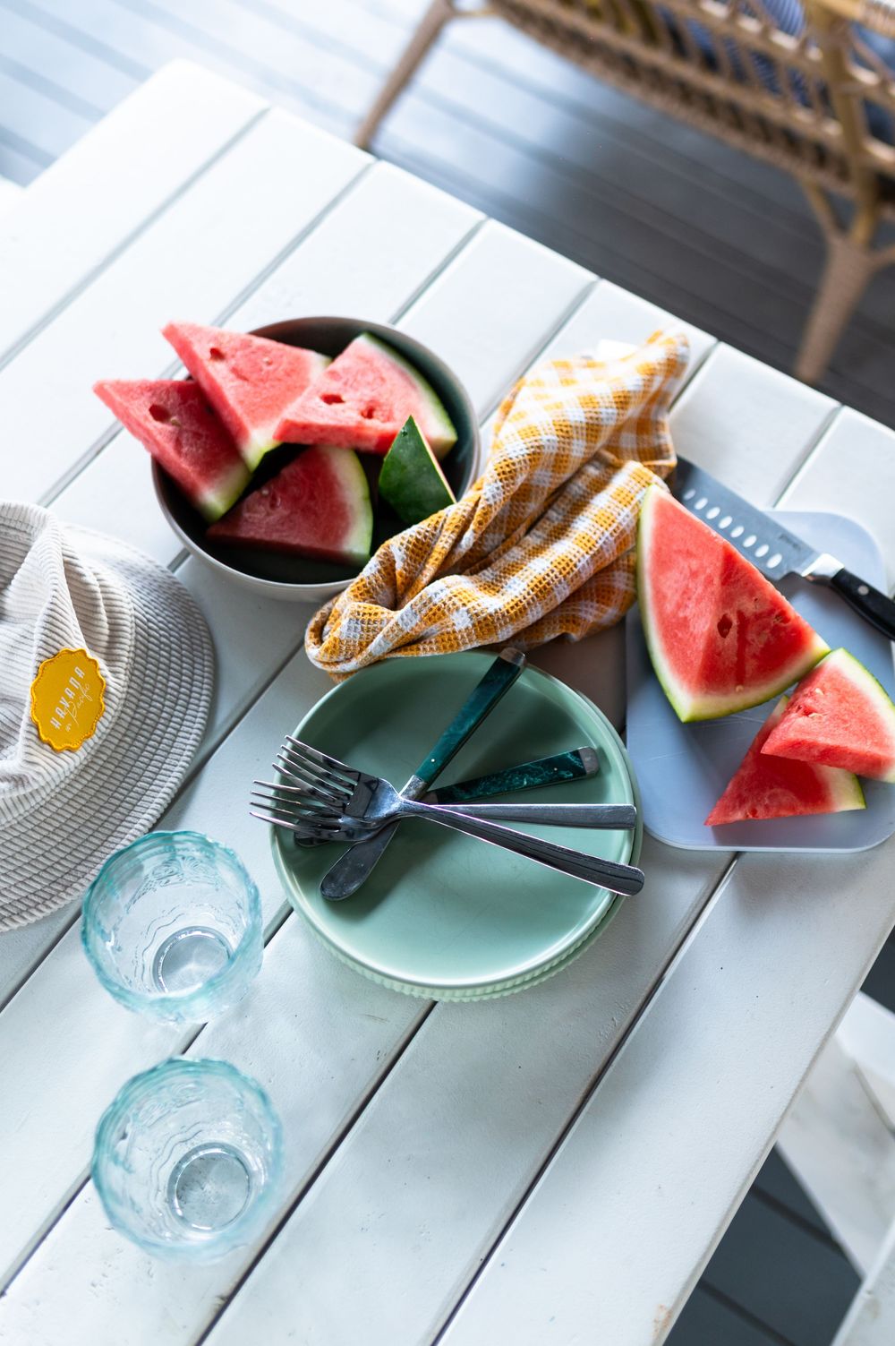 Fresh watermelon slices served on a white outdoor table with plates, forks, and blue glassware.