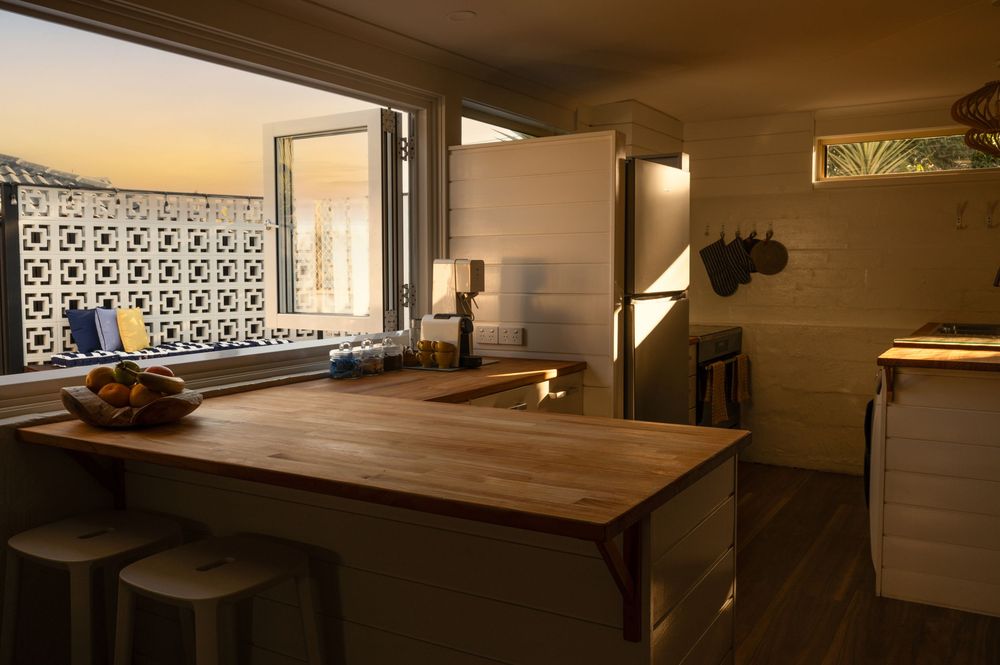 Warm kitchen interior with wooden island countertop, bar stools, and decorative window at sunset.