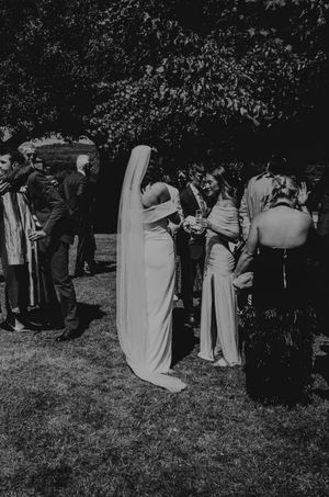 Black and white photo of a bride in a veil mingling with guests outdoors at a wedding reception.