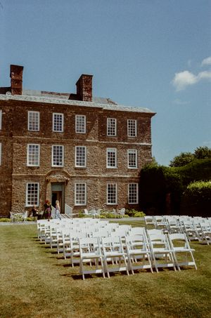 White chairs arranged on lawn before a grand historic brick manor house for an outdoor wedding ceremony.