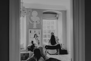 Black and white photo of two women in a elegantly decorated room, captured through a doorway during bridal preparations.