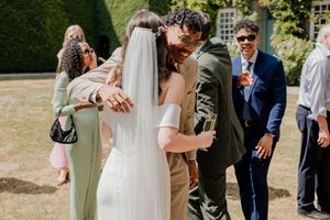 Bride and groom share a warm embrace with wedding guests outdoors at a sunny garden venue.