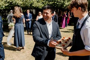 Guest laughing while server offers appetizers on a tray at an outdoor wedding reception.