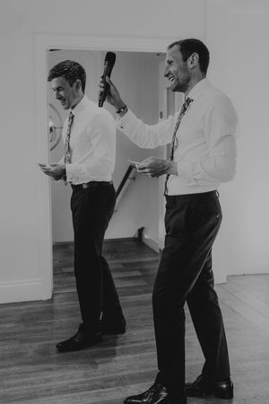 Black and white photo of man holding microphone giving wedding speech reflected in mirror.