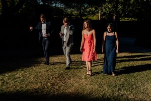 Four elegantly dressed wedding guests walking across sunlit grass at an outdoor summer wedding reception.