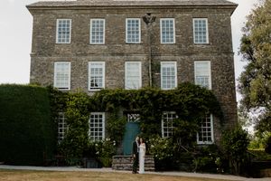 Wedding couple posing before a grand ivy-covered stone manor house with teal front door.