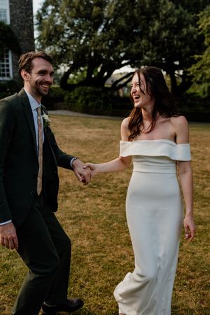 Happy bride and groom holding hands and laughing outdoors on their wedding day.