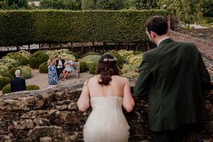 Bride and groom overlooking wedding guests in a beautiful formal garden with manicured hedges.