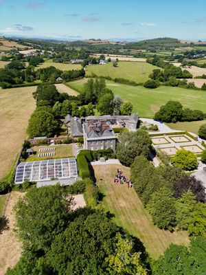 Aerial view of a grand country estate surrounded by lush green fields and gardens in the English countryside.