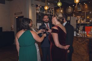 Guests in formal attire socializing and drinking wine at an elegant indoor wedding reception bar.