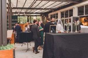 Wedding guests mingling at an outdoor reception venue with black draped tables and string lights.
