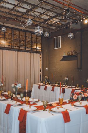 Elegant wedding reception venue with disco balls, rust-colored linens, candles, and floral centerpieces.