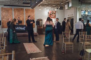 Wedding reception guests mingling and dancing in stylish industrial venue with string lights and gold chairs.