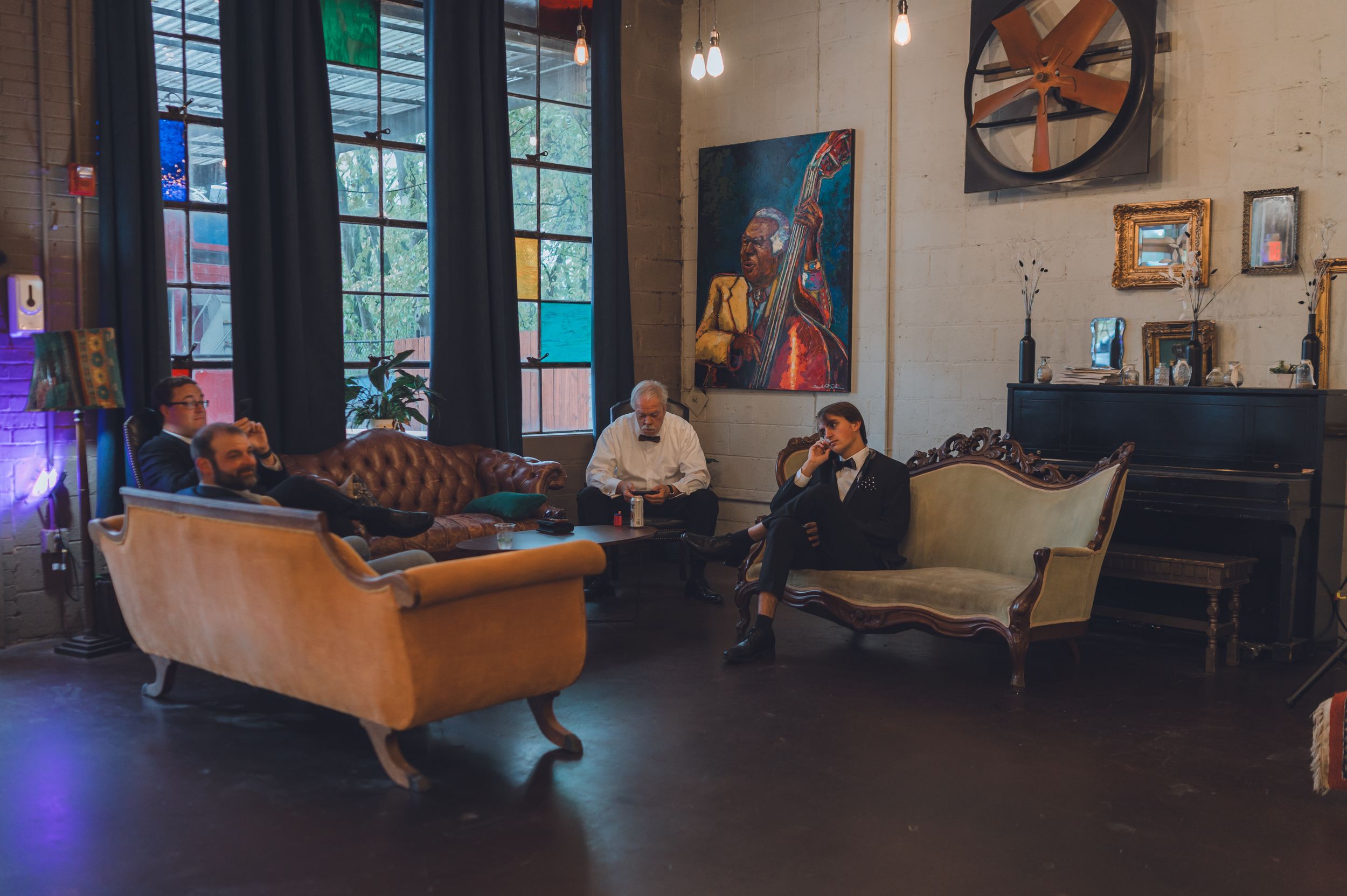 Three men relax on vintage sofas in a rustic industrial venue with colorful artwork on the walls.