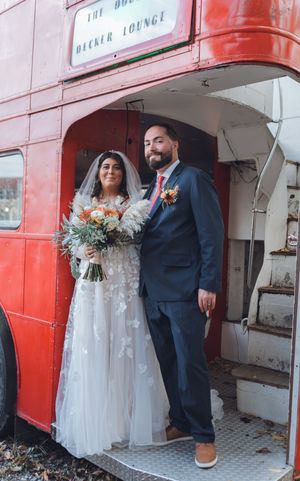 Bride and groom posing at the entrance of a vintage red double-decker bus on their wedding day.
