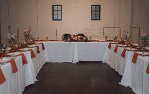 Elegant U-shaped banquet table with white linens and burnt orange napkins set for a formal event in a rustic venue.