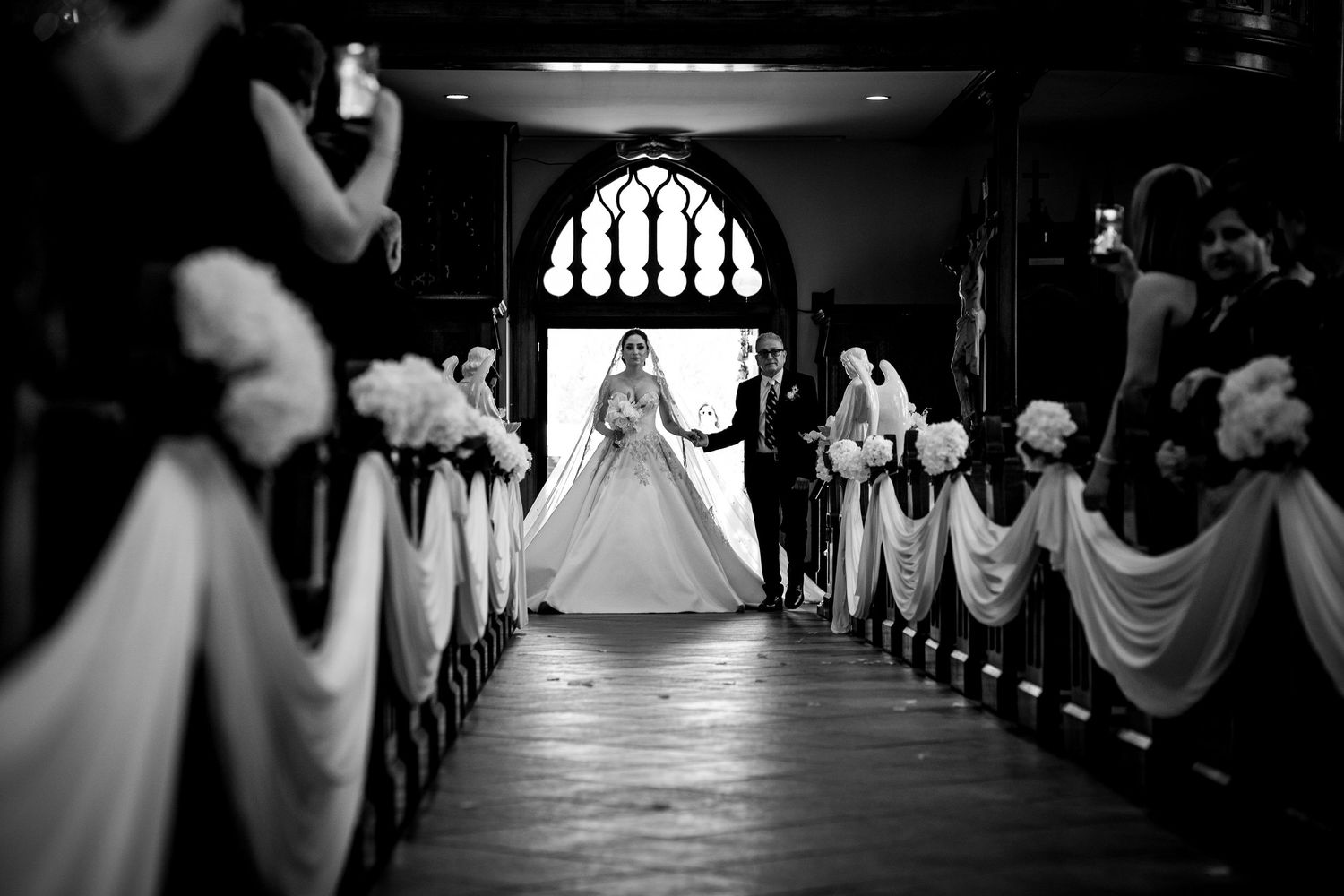 Black and white photo of a bride walking down the church aisle toward the altar on her wedding day.