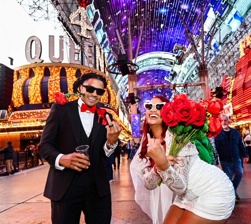 Couple in formal attire posing at Fremont Street Experience in Las Vegas, holding roses and drinks.