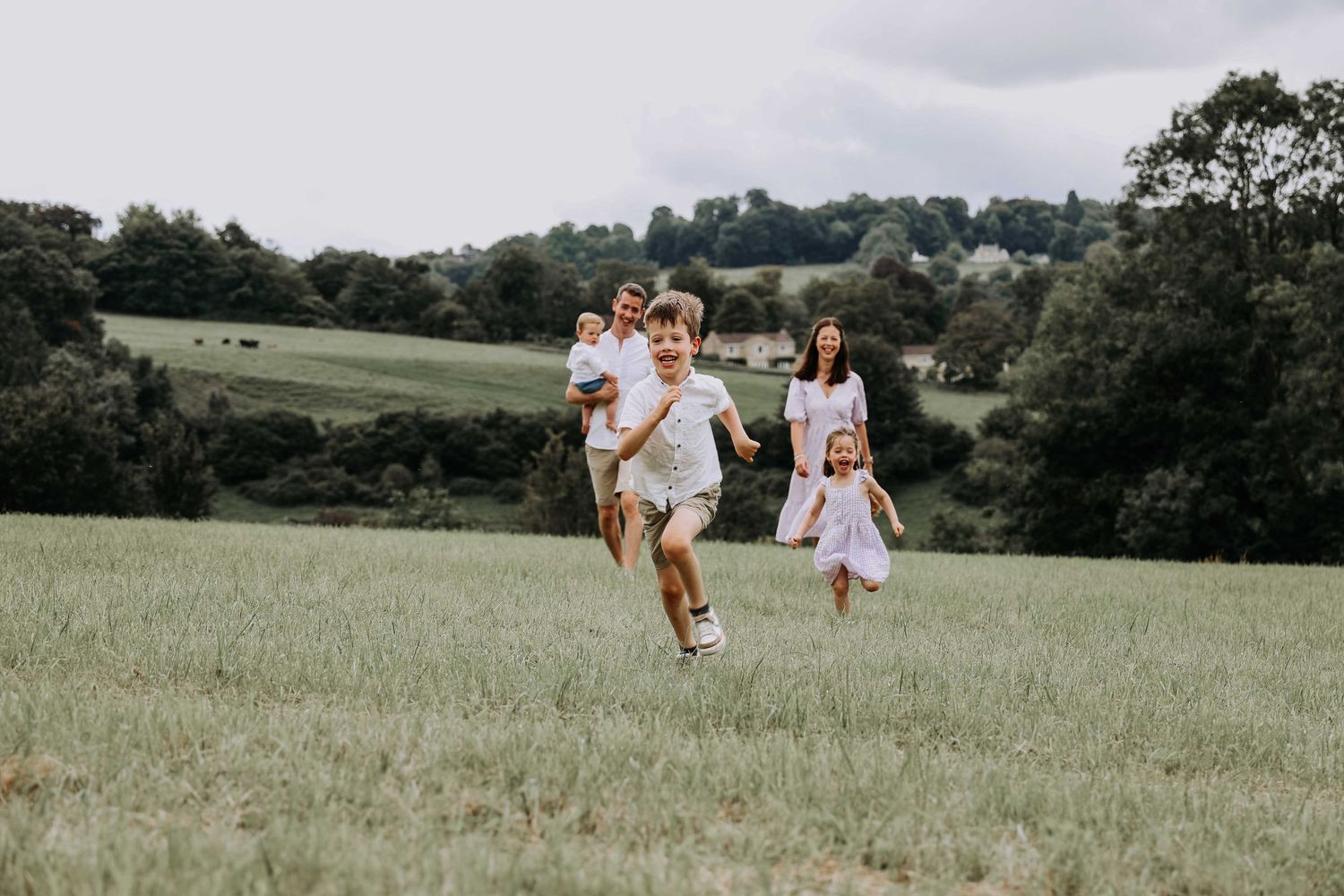 Children running across a countryside field with their parents during a relaxed family photography session.