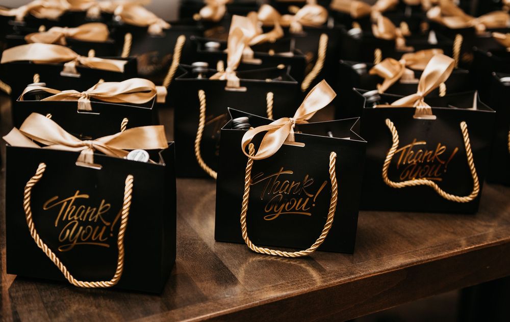 Black gift bags with gold rope handles and thank you ribbons arranged on a table for a wedding or event.