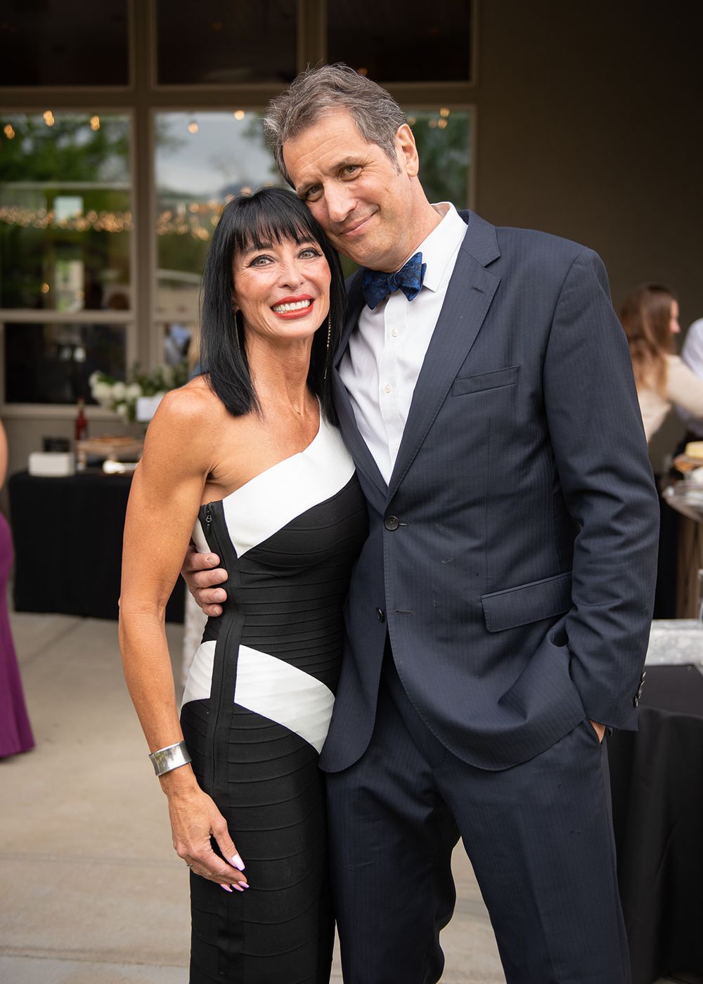 Elegant couple posing at formal event, woman in black and white dress, man in navy suit with bow tie.