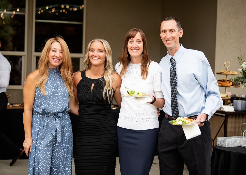Four smiling adults posing together at an elegant outdoor social gathering event.