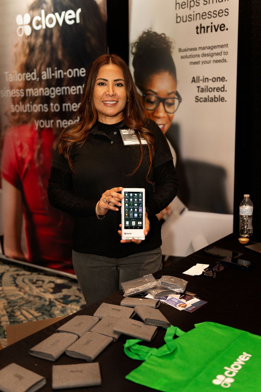 A woman smiles holding a Clover POS device at a Clover business solutions trade show booth.