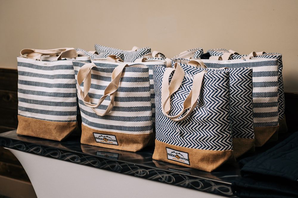 Four striped and chevron canvas tote bags with leather bottoms displayed on a dark surface.