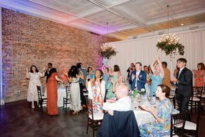 Wedding reception guests celebrating in a brick-walled venue with floral chandeliers and colorful attire.