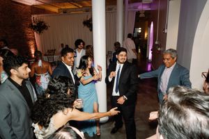 Guests dancing and celebrating at an elegant indoor wedding reception with white columns and warm ambient lighting.
