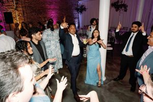 Guests dancing joyfully at an elegant wedding reception with purple lighting and white columns.