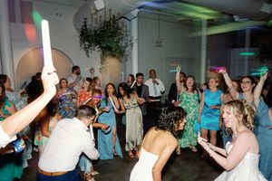 Guests dancing and celebrating at a lively wedding reception, waving glow sticks and colorful accessories on the dance floor. NC Wedding