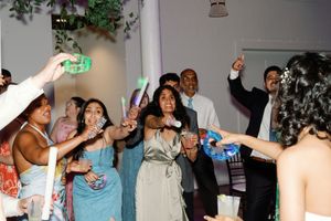 Excited wedding guests dancing and celebrating with glow sticks at a lively indoor wedding reception.