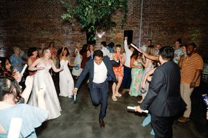 Guest dancing energetically at wedding reception with brides and guests cheering at The Elia wedding venue. Booth Creative Co.