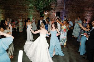 Brides dancing joyfully with guests in elegant gowns at lively wedding reception. Wedding Photographer in Wilmington NC