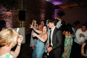 Wedding guests dance and celebrate joyfully at a lively indoor reception with brick walls and colorful lighting. Wilmington NC Wedding Photo