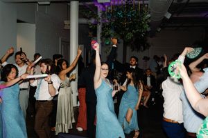 Guests dancing joyfully at wedding reception party in venue with purple lighting and decorations. Wilmington NC Wedding Photography