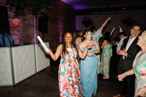 Guests dancing joyfully at an indoor wedding reception, woman in floral dress holding a glow stick. Wilmington NC Wedding Venue
