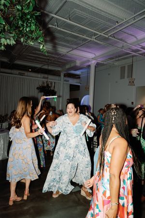 Guests dancing joyfully at a wedding reception in a decorated venue with purple lighting and greenery. Wilmington, NC Wedding Photography