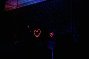 Two red neon heart shapes glowing on a dark brick wall in a dimly lit room. Wedding Reception Decor at The Elia in Wilmington, NC