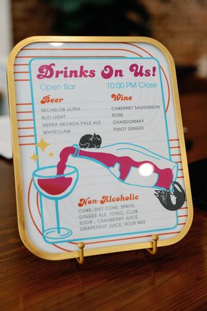 Gold-framed wedding open bar sign listing beer, wine, and non-alcoholic drinks with colorful retro design, closing at 10PM.
