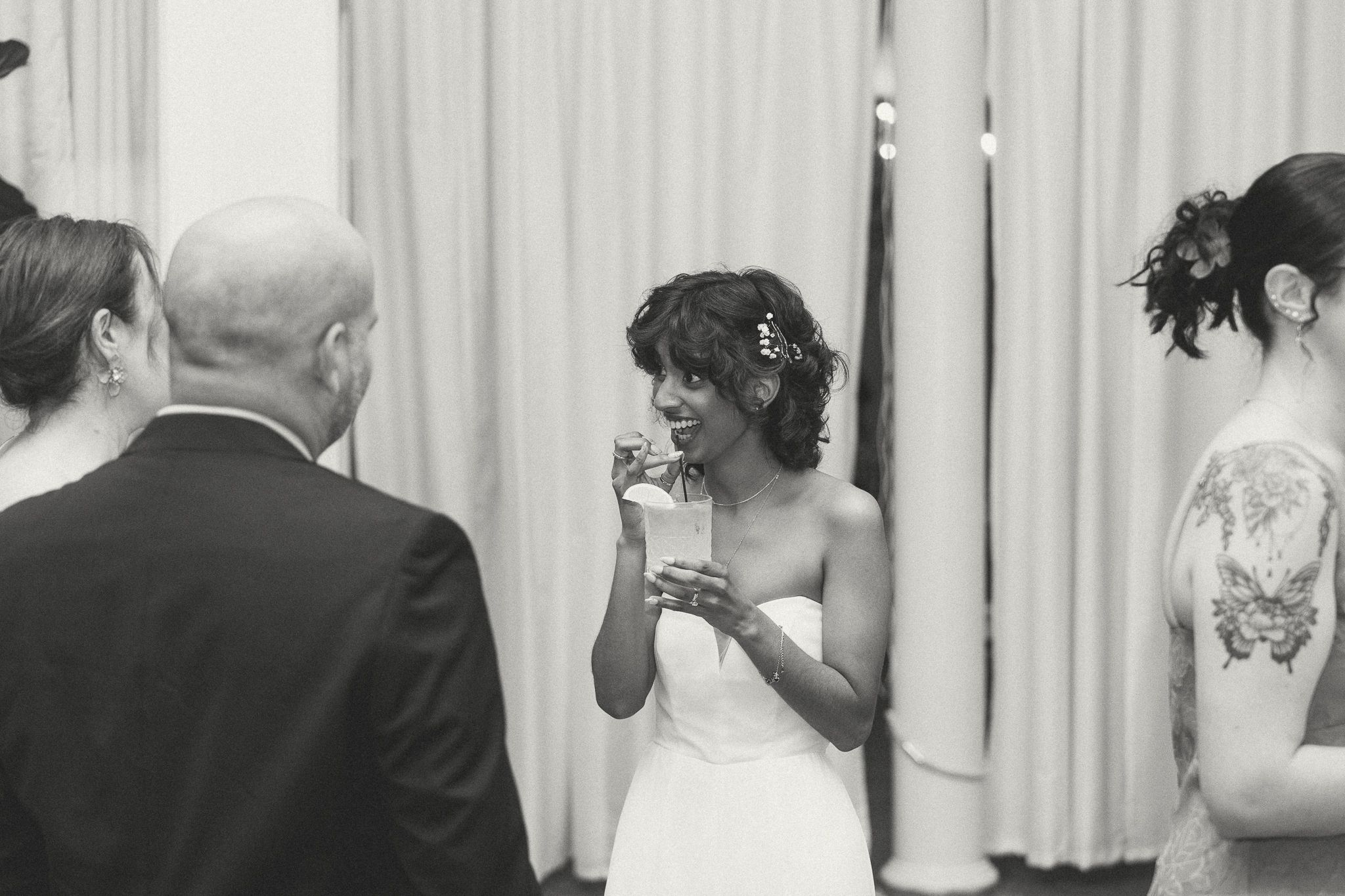 Bride laughing and holding a drink at wedding reception in black and white photo.